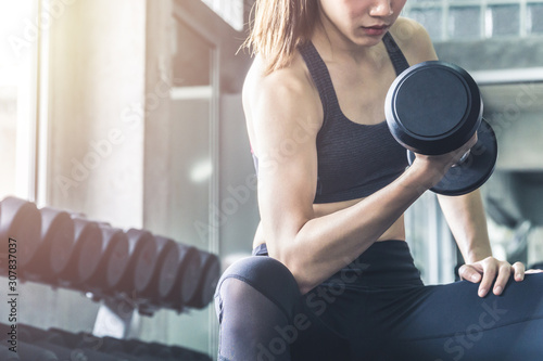 Muscular athletic woman in sports bra lifting dumbbell at the gym.