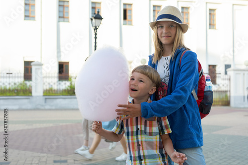 Happy kids, brother and sister holding cotton candy on street in sunny day © Olya