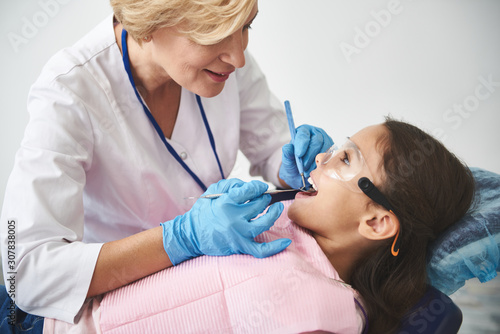 Professional female dentist treating kids teeth with pleasure