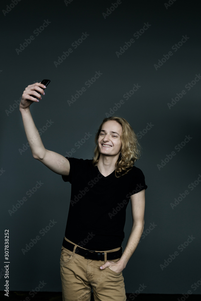 Young man with long blonde hair takes a selfie on a black background. Young man with long blonde hair takes a selfie on a black background.