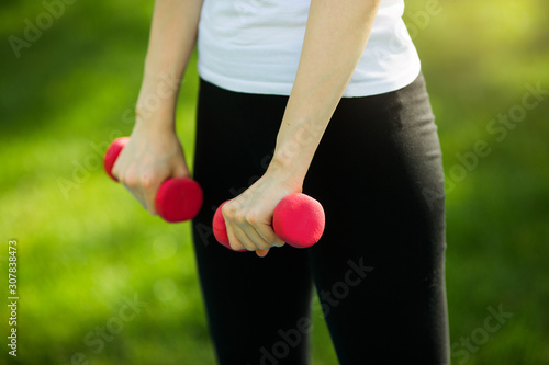 dumbbells in the hands of a young woman in a park