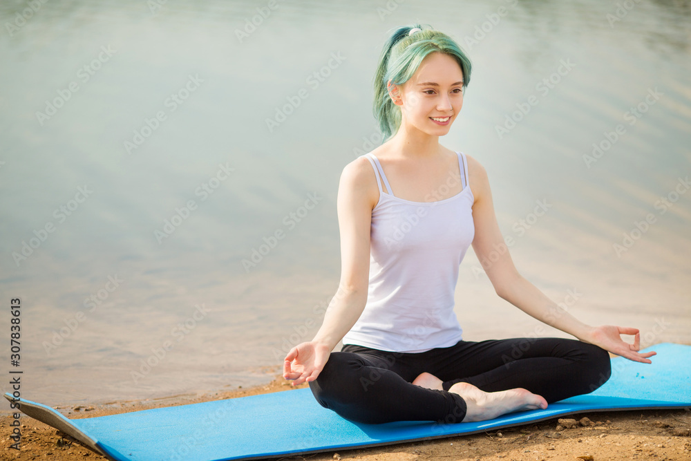 Fototapeta premium beautiful young woman practices yoga near the lake