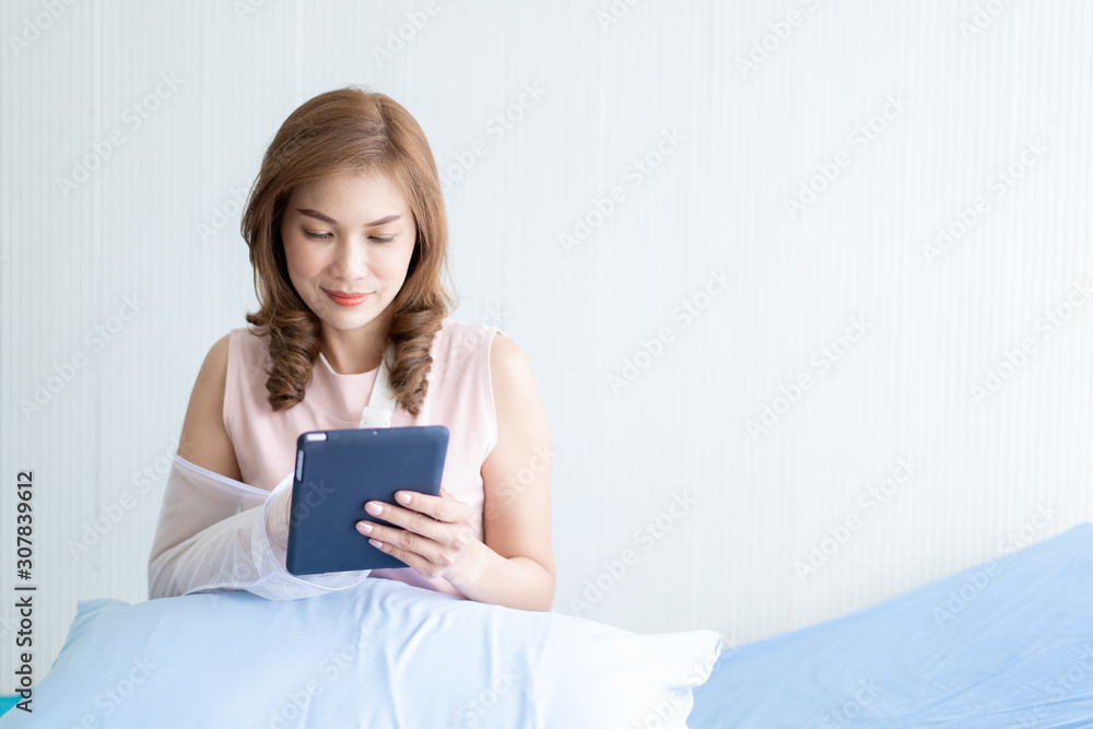 Asian woman broken arm sitting on the bed in hospital using a tablet. Concept of healthcare in modern lifestyle. Photograph with copy space. Asian woman broken arm sitting on the bed in hospital using a tablet. Concept of healthcare in modern lifestyle. Photograph with copy space.