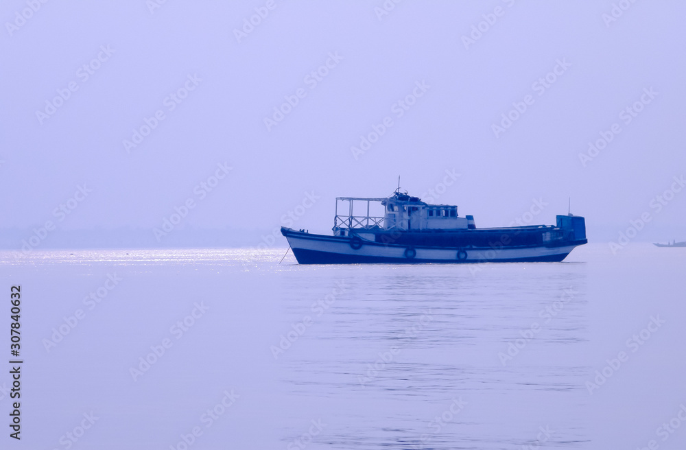 A Small Commercial Fishing trawler (nautical vessel) on river inland water before heading out to Bay of Bengal. Late evening view with rural background. Fishing hub, Digha Mohona, West Bengal, India.