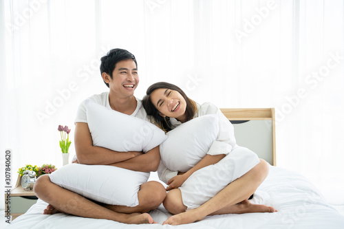 Funny and romantic Asian couple' portrait in bedroom with natural light from window, concept of relationship between husband and wife and being a family. © DG PhotoStock