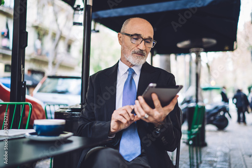 Elderly focused businessman in glasses texting on tablet