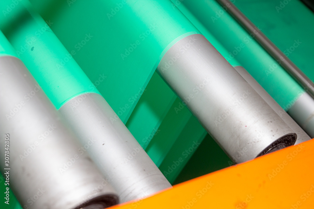 Imagery of Yellow spool of plastic packaging sheet heavy duty for industrial use outdoors wrapped around a worn metal pole ready to feed into Orange machine for cutting into shape or printing logos Imagery of Yellow spool of plastic packaging sheet heavy duty for industrial use outdoors wrapped around a worn metal pole ready to feed into Orange machine for cutting into shape or printing logos