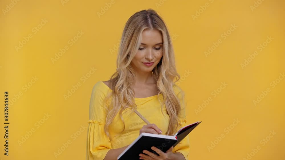 smiling woman writing in notebook isolated in yellow smiling woman writing in notebook isolated in yellow