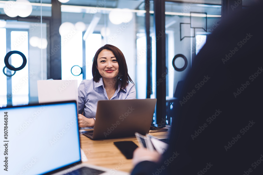 Smiling ethnic woman working at laptop and looking at camera in office Smiling ethnic woman working at laptop and looking at camera in office
