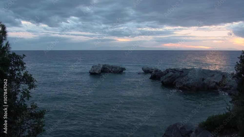 view of the calm sea with a rocky shore at sunset in the evening with a cloudy sky view of the calm sea with a rocky shore at sunset in the evening with a cloudy sky