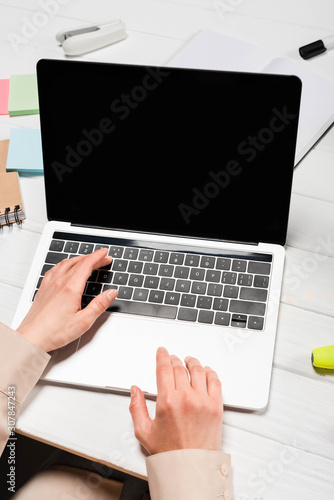 cropped view of woman using laptop at workplace with office supplies