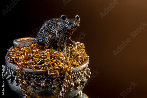 Composition from metal figures: a rat sits in a pot of gold. Copy space for text. Concept for the zodiac calendar in 2020. Symbol of well-being and prosperity and wealth. Black background