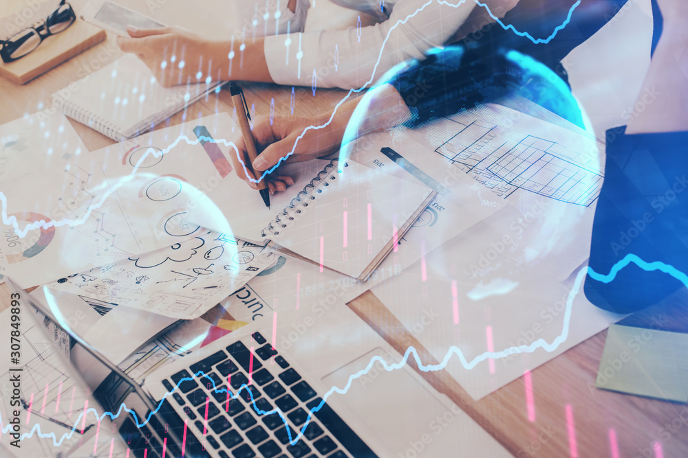 A woman hands writing information about stock market in notepad. Forex chart holograms in front. Concept of research. Double exposure A woman hands writing information about stock market in notepad. Forex chart holograms in front. Concept of research. Double exposure