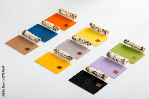 multicolored credit card templates near cash rolls with dollar banknotes isolated on white