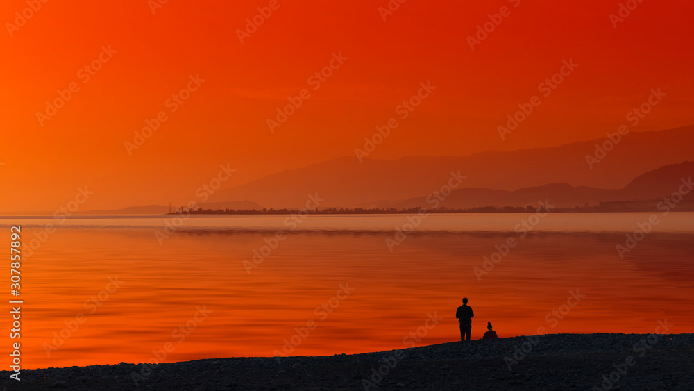 Seascape with orange sunset and silhouettes of people.