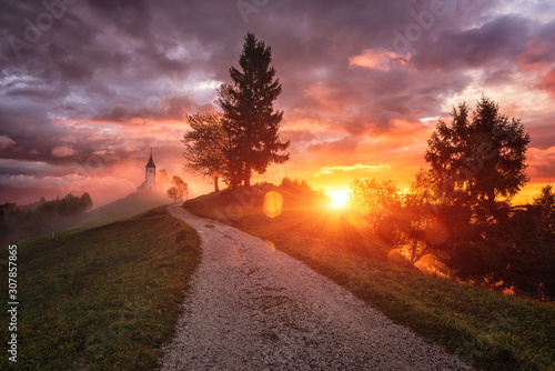 Jamnik church St Primus and Felician at sunrise, Slovenia. Amazing landscape with foot path to the church on hill side, dramatic cloudy sky and rising sun, travel background, famous tourist attraction