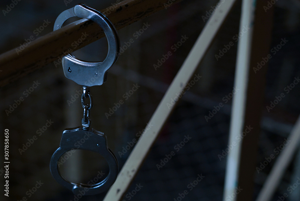 Black and white Handcuffs on the handrail on a prison or arrest background. Concept: problems with the law, criminal, offenses, waiting for the verdict of the judge, balancing on the border of the law Black and white Handcuffs on the handrail on a prison or arrest background. Concept: problems with the law, criminal, offenses, waiting for the verdict of the judge, balancing on the border of the law
