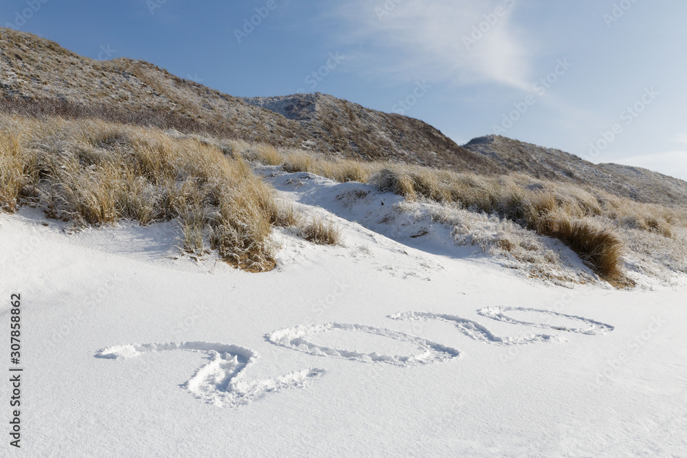 Happy New Year 2020 text in snow on the beach with dunes in snow as background