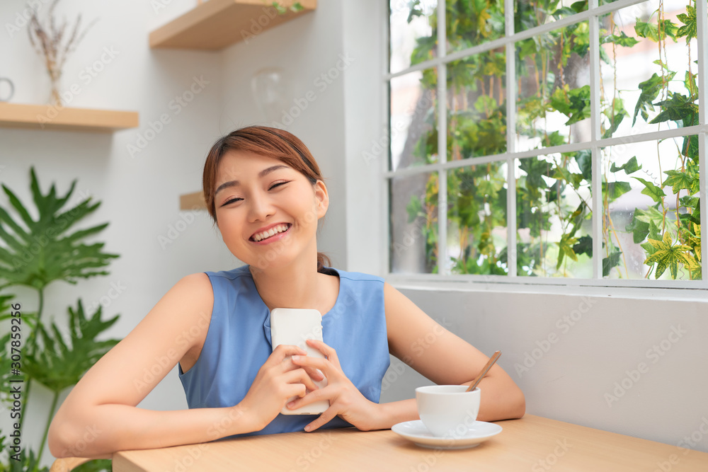 Happy young Asian woman smiling while using phone and drinking coffee Happy young Asian woman smiling while using phone and drinking coffee