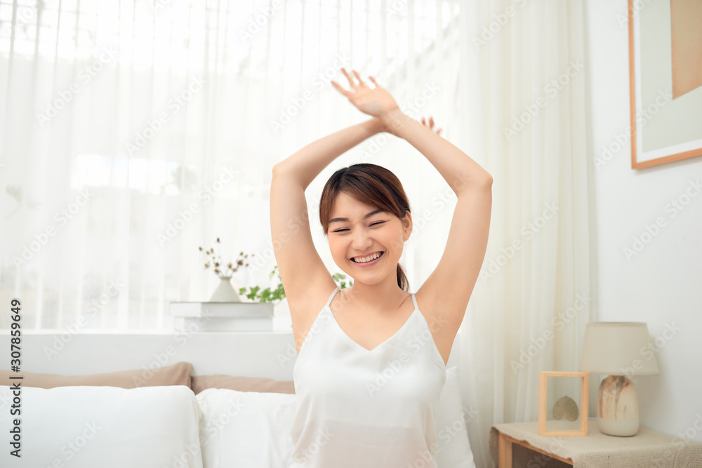 Happy Asian girl waking up stretching arms sitting on the bed in the morning Happy Asian girl waking up stretching arms sitting on the bed in the morning