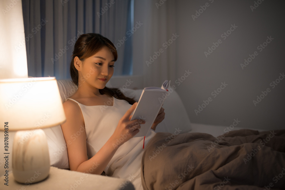 leisure and people concept - young woman reading book in bed at night home leisure and people concept - young woman reading book in bed at night home