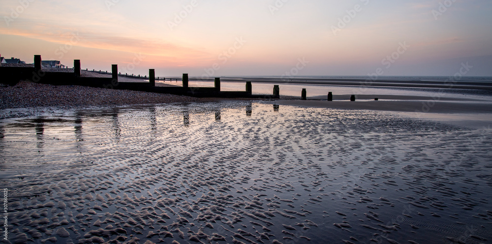 Timber groynes and reflections at dawn, Camber Sands, Sussex, England