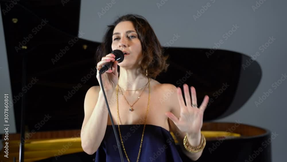 A girl in a blue jumpsuit sings into a microphone against the background of the piano A girl in a blue jumpsuit sings into a microphone against the background of the piano