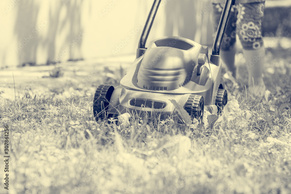 Deatil of plastic toy lwn mower with child pushing it. - obrazy, fototapety, plakaty 