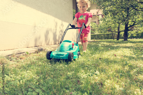 Cute girl lawn mowing with plastic toy mower. photo