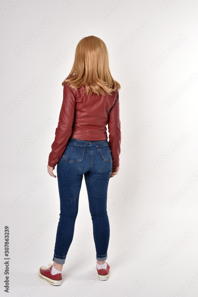Full length portrait of a pretty blonde girl wearing red leather jacket denim jeans and sneakers. Standing pose, facing away from the camera, on a studio background. Full length portrait of a pretty blonde girl wearing red leather jacket denim jeans and sneakers. Standing pose, facing away from the camera, on a studio background.