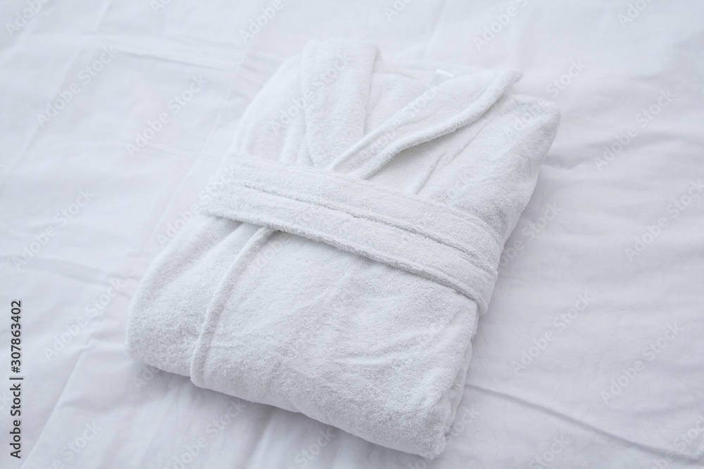 Clean folded bathrobe on white bed. - obrazy, fototapety, plakaty 