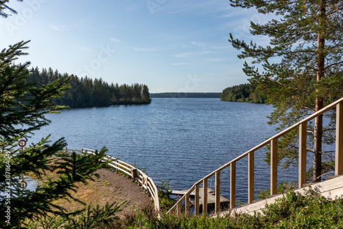 Wooden stairs railing with great view on finish river and pine trees forest with beautiful sky landscape. Recreation area on river.