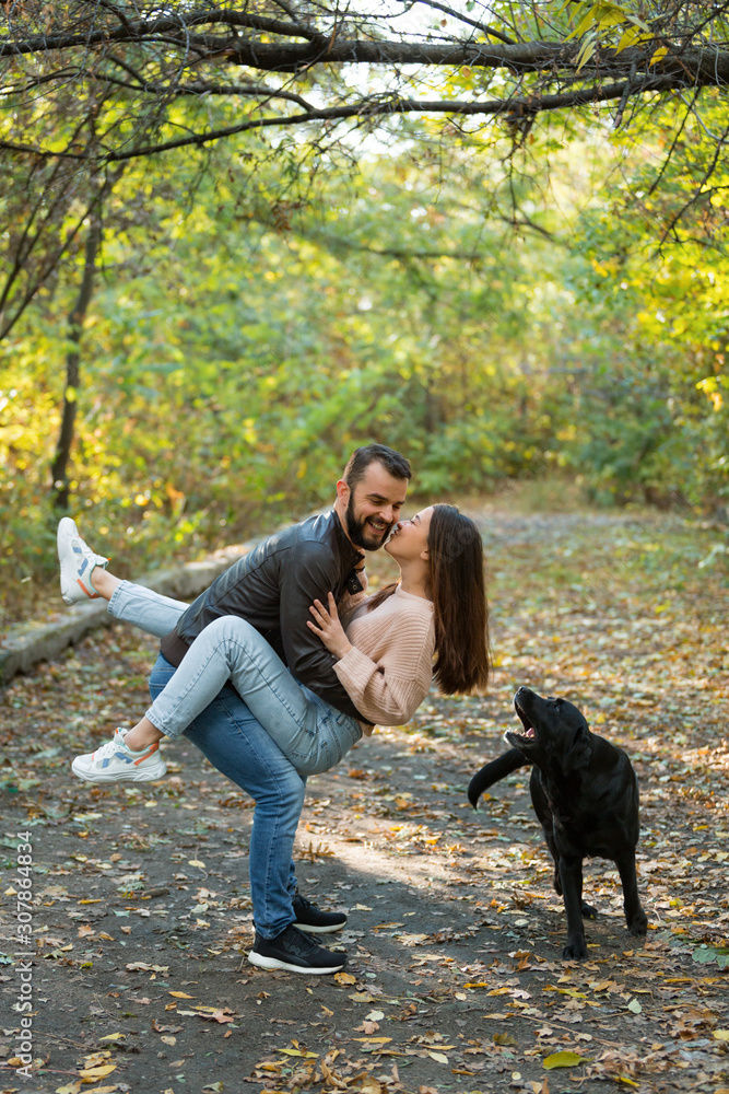 A young beautiful couple and their labrador in the Park. A man holds a woman in his arms. Warm autumn evening in the forest.