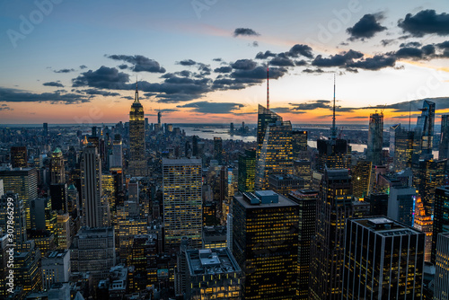 Aerial view of skyscrapers and towers in midtown skyline of Manhattan with evening sunset sky. Scenery cityscape of financial district with famous New York Landmark  illuminated Empire State Building