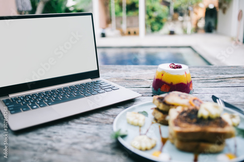 Working laptop and jelly near plate with sandwich on table