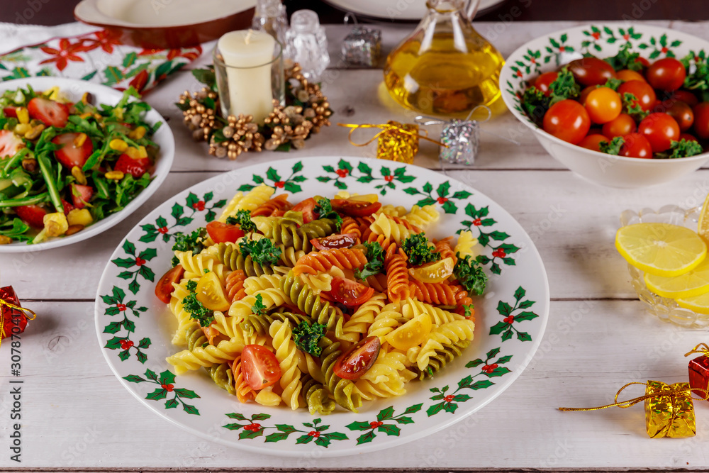 Festive christmas dinner with colorful pasta, cherry tomatoes, salad on white wooden table. Festive christmas dinner with colorful pasta, cherry tomatoes, salad on white wooden table.
