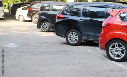 Closeup of rear, back side of red car with other cars parking in outdoor parking area in sunny day.