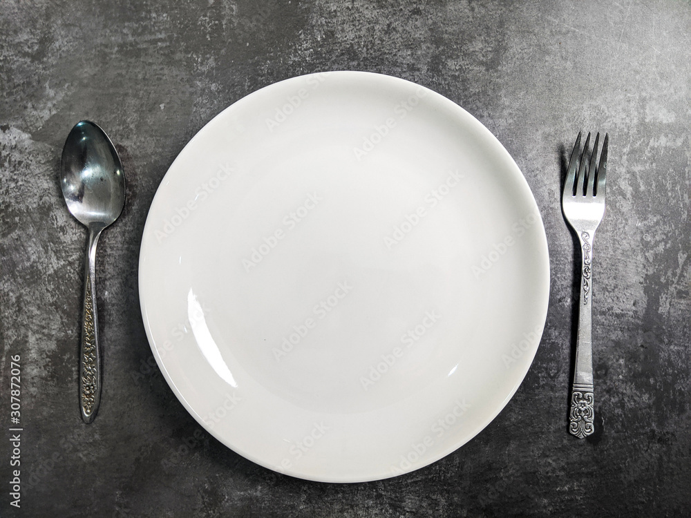 Empty White ceramic plate with fork and spoon on gray stone concrete table background. Copy space. Menu Recipe Concept Empty White ceramic plate with fork and spoon on gray stone concrete table background. Copy space. Menu Recipe Concept