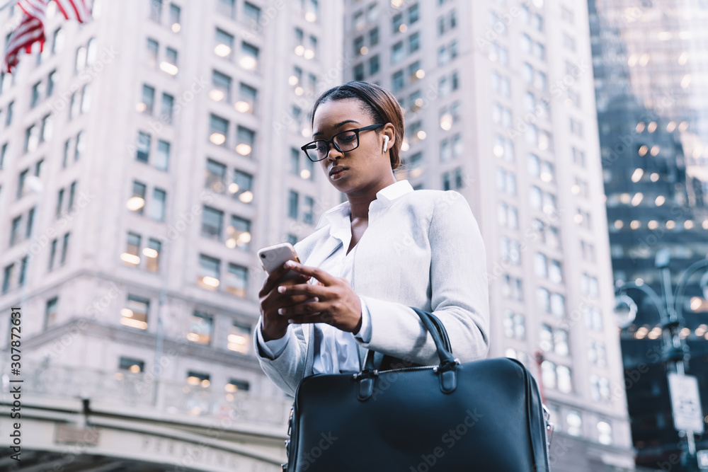 Focused black executive woman texting on smartphone in city Focused black executive woman texting on smartphone in city