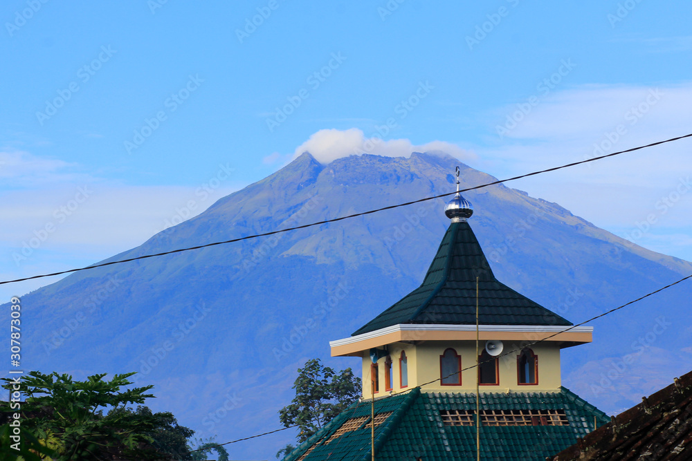 The peak of Mount Sumbing with a mosque dome as the foreground with a Javanese traditional architectural style, equipped with loudspeakers.