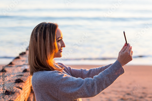 Pretty Woman at the beach during Sunset taking a Selfie