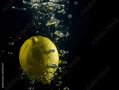 lemon falls into the water with air bubbles over black background © Анастасия Жукова