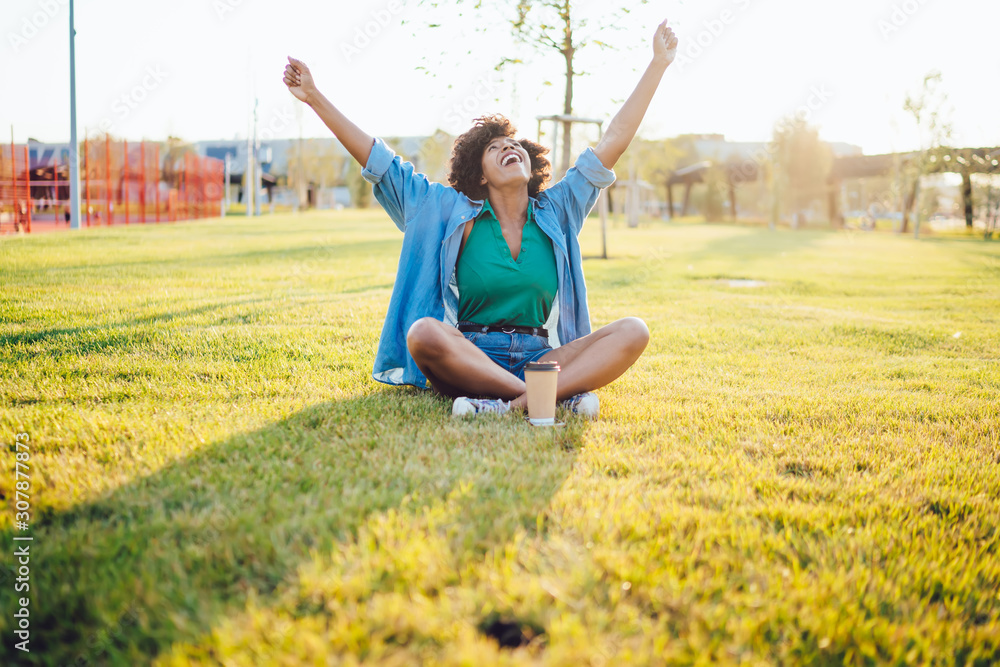 Happy overjoyed african american hipster girl feeling carefree and excited recreating on green grass, emotional dark skinned woman amazed with good mood and sunny weather on weekends in city park Happy overjoyed african american hipster girl feeling carefree and excited recreating on green grass, emotional dark skinned woman amazed with good mood and sunny weather on weekends in city park