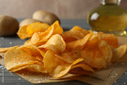 Potato crispy chips on craft paper  sault  oliv oil  potato on gray wooden background  space for text. Closeup