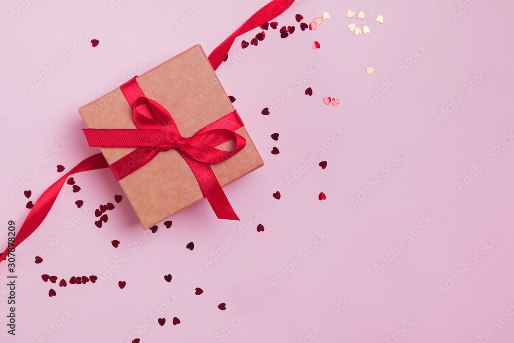 Gift box decorated with red bow on pink background with heart shape glitter confetti. Gift box decorated with red bow on pink background with heart shape glitter confetti.