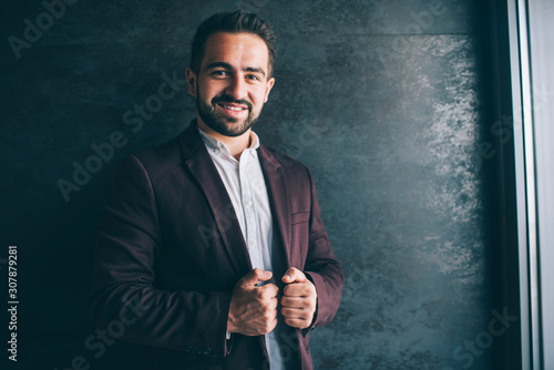 Portrait caucasian male entrepreneur in trendy stylish outfit standing indoors enjoying luxury lifestyle, successful businessman dressed in stylish clothes posing near promotional background.