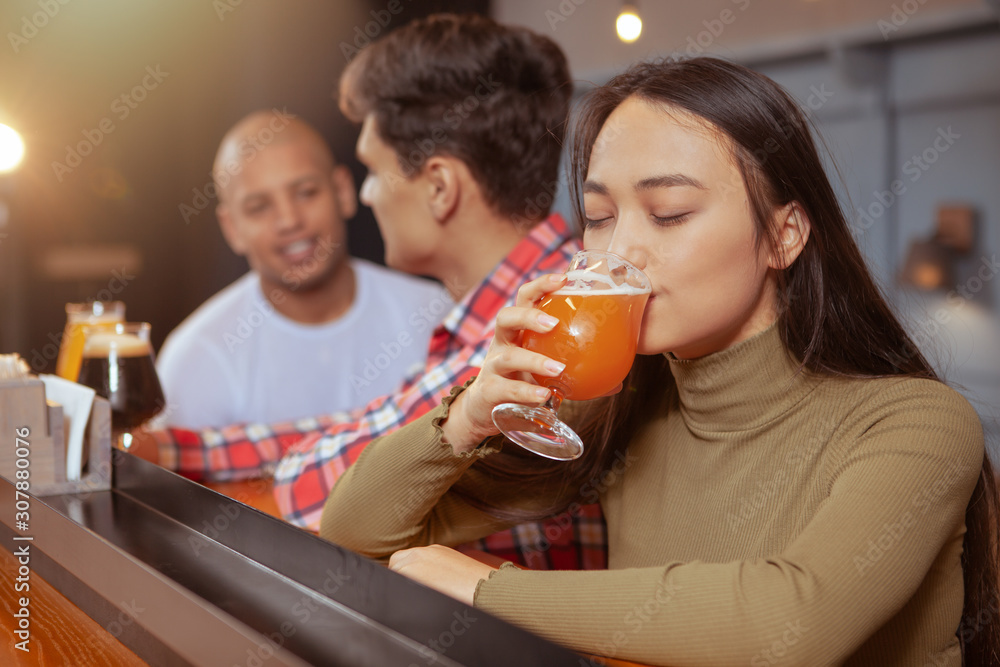 Young Asian woman enjoying drinking delicious beer at the pub with her friends Young Asian woman enjoying drinking delicious beer at the pub with her friends