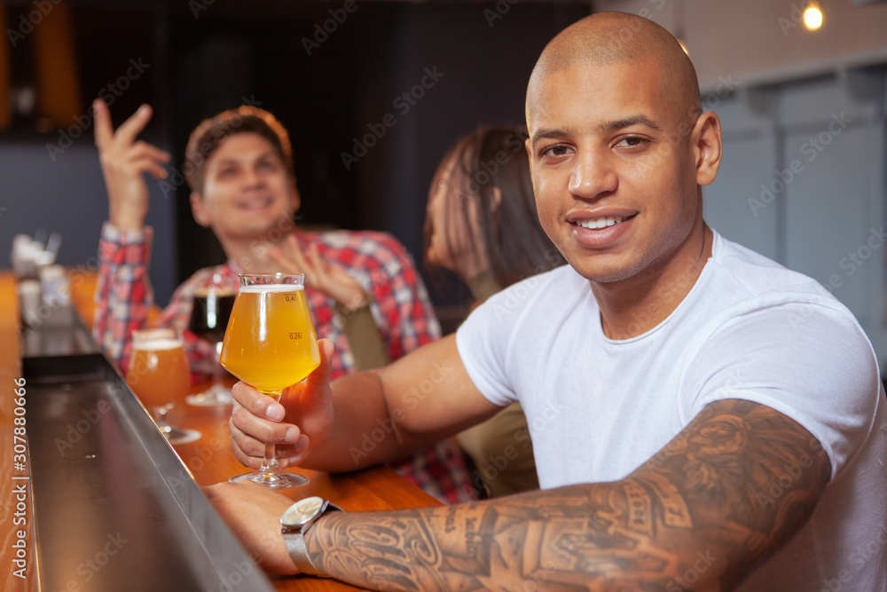 Handsome African man smiling to the camera, holding beer glass, relaxing at the pub