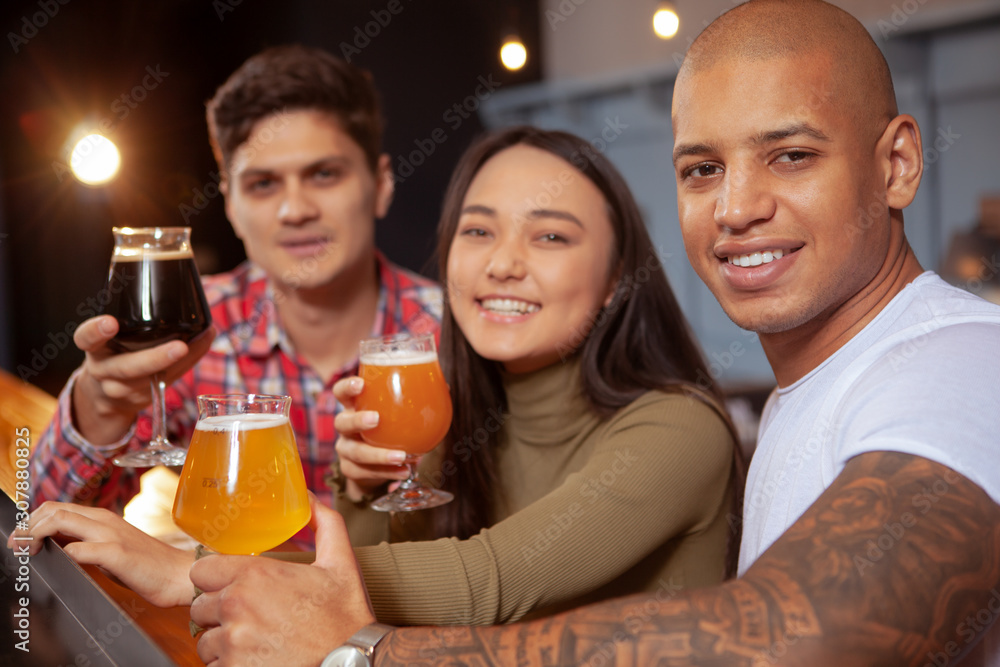 Group of young happy friends smiling to the camera, holding their beer glasses, relaxing together at the local pub Group of young happy friends smiling to the camera, holding their beer glasses, relaxing together at the local pub