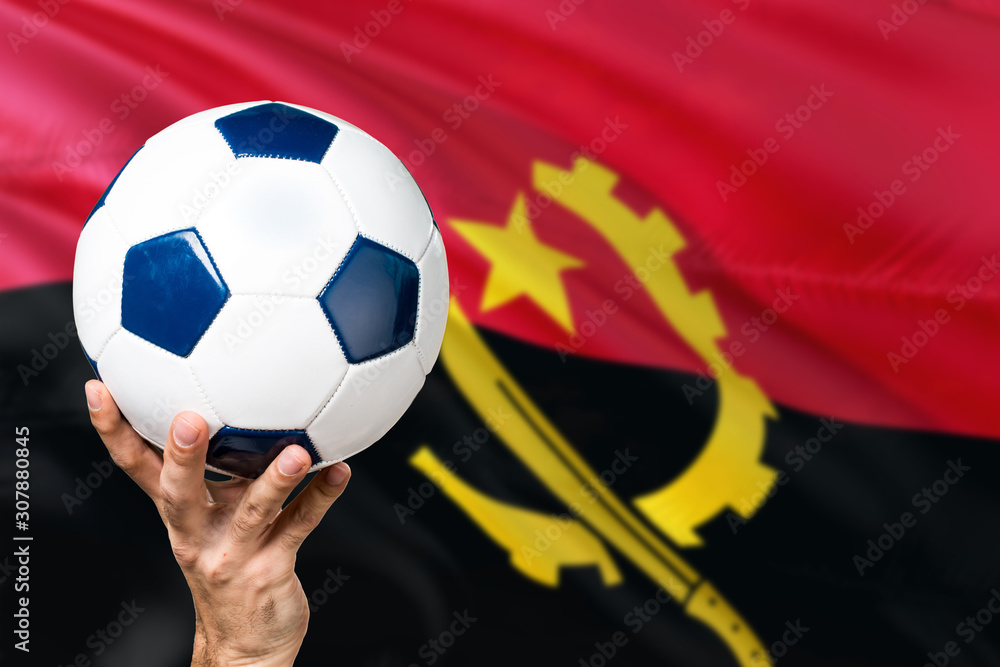 Naklejka premium Angola soccer concept. National team player hand holding soccer ball with country flag background. Copy space for text.